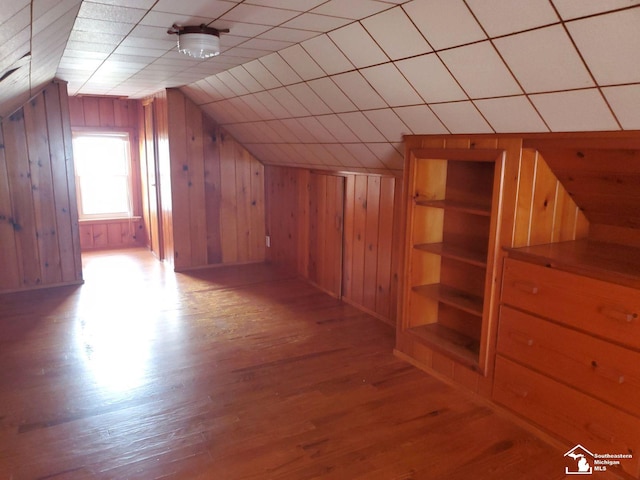 additional living space with built in shelves, light hardwood / wood-style flooring, lofted ceiling, and wood walls