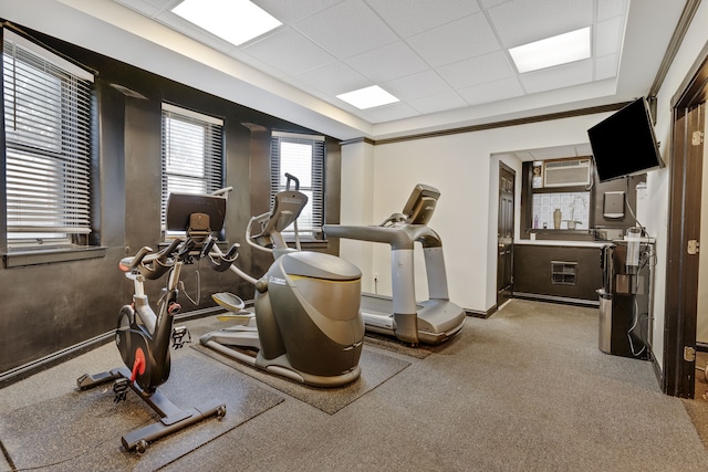 exercise area featuring light carpet, an AC wall unit, and a drop ceiling