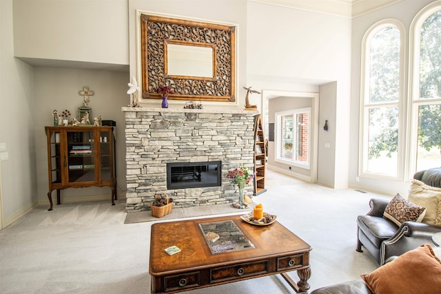 carpeted living room featuring a stone fireplace, a wealth of natural light, and ornamental molding