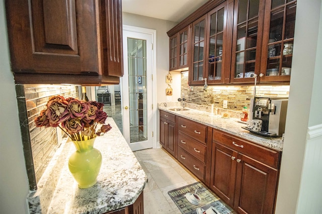 kitchen featuring sink, tasteful backsplash, light stone counters, dark brown cabinets, and light tile patterned floors