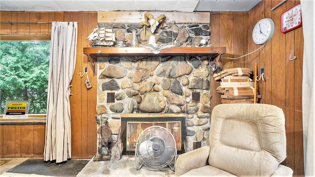 living area with concrete floors, a stone fireplace, and wood walls