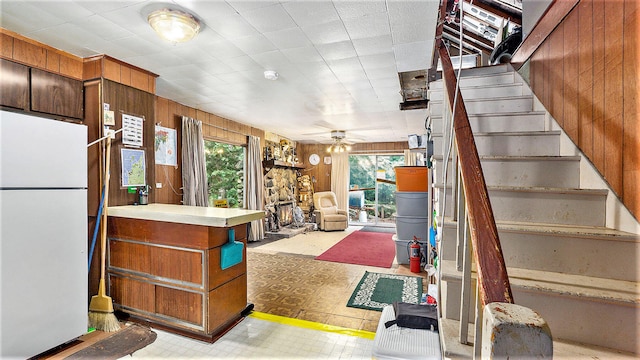 interior space featuring ceiling fan, white fridge, a fireplace, and wooden walls