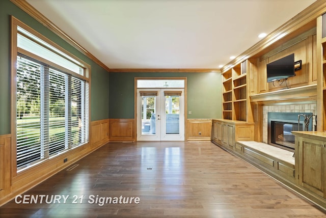 unfurnished living room with hardwood / wood-style flooring, a fireplace, crown molding, and french doors