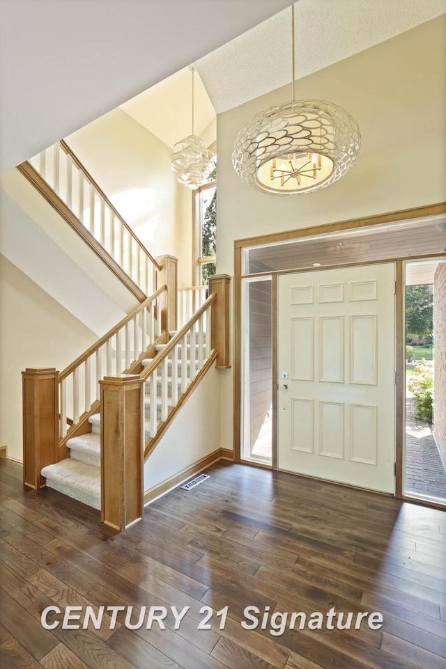 foyer entrance featuring high vaulted ceiling, dark wood-type flooring, and a notable chandelier