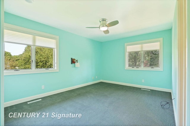 empty room with ceiling fan, a healthy amount of sunlight, and dark carpet