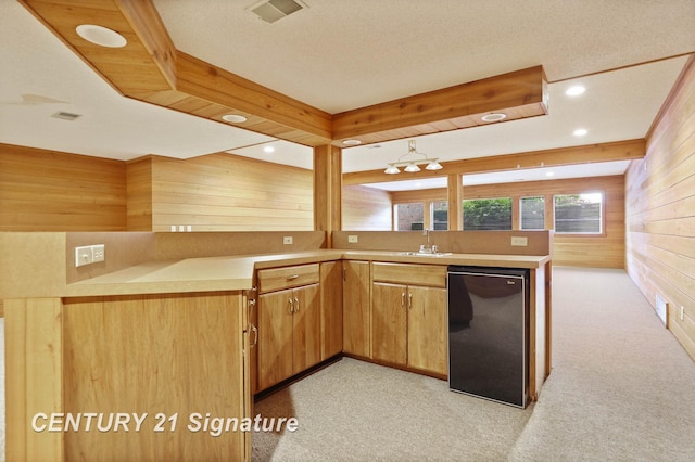 kitchen with sink, kitchen peninsula, light colored carpet, a textured ceiling, and wooden walls