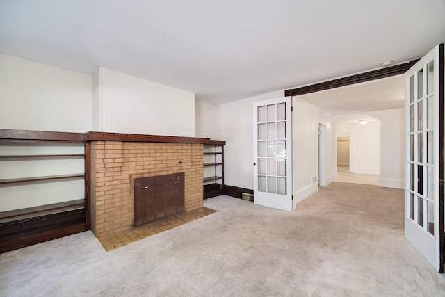 unfurnished living room with light colored carpet, a fireplace, and french doors