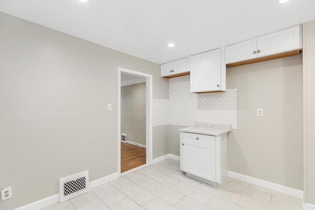 kitchen with light stone countertops, white cabinetry, backsplash, and light tile patterned floors