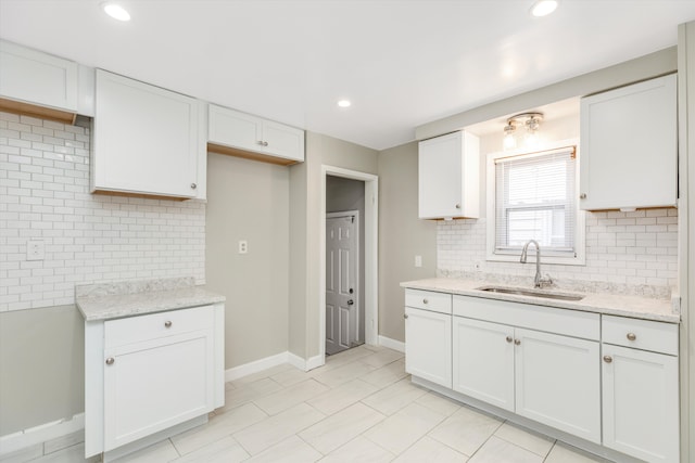 kitchen with light stone counters, white cabinetry, and sink