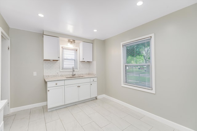 kitchen featuring tasteful backsplash, white cabinetry, sink, and light stone countertops