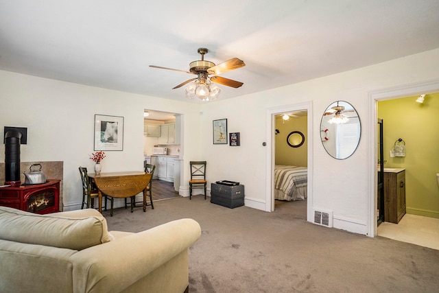 carpeted living room featuring a wood stove and ceiling fan