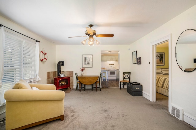 interior space with carpet flooring, a wood stove, and ceiling fan