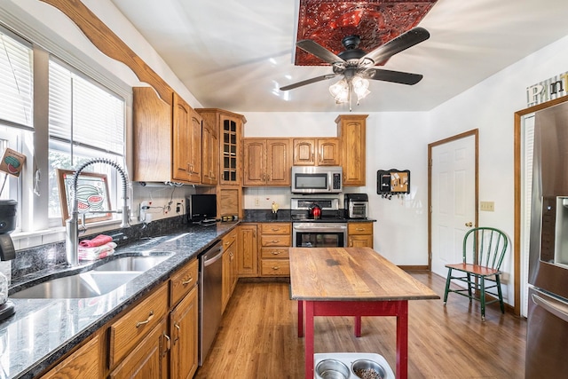 kitchen with dark stone countertops, sink, stainless steel appliances, and light hardwood / wood-style floors