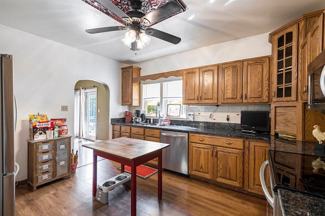 kitchen featuring ceiling fan, stainless steel appliances, dark stone countertops, wood-type flooring, and decorative backsplash