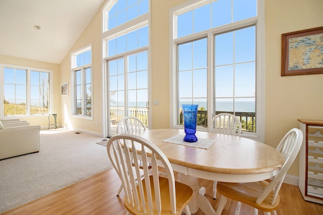 dining space featuring plenty of natural light, a water view, high vaulted ceiling, and hardwood / wood-style flooring