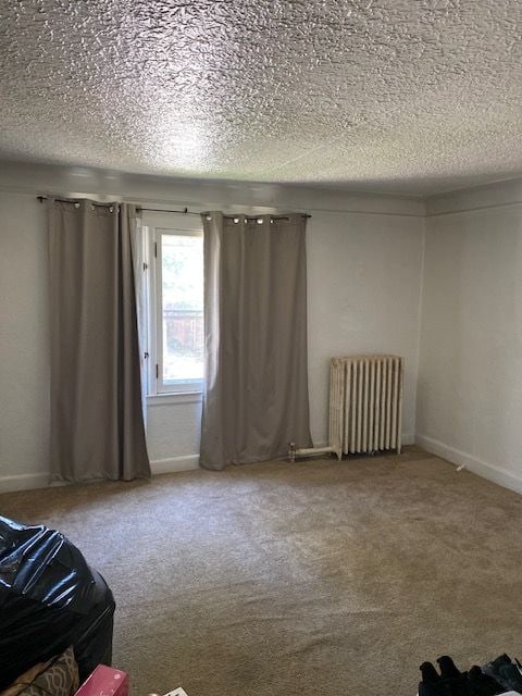 carpeted empty room with a textured ceiling and radiator