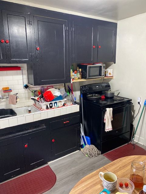 kitchen with tile counters, sink, black electric range oven, backsplash, and light hardwood / wood-style floors