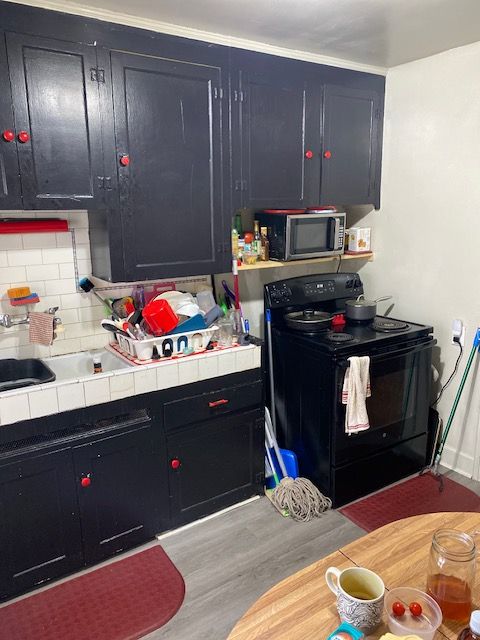 5051 Bishop St, Detroit, MI 48224 - kitchen with electric range, tile counters, stainless steel microwave, light wood-type flooring, and decorative backsplash