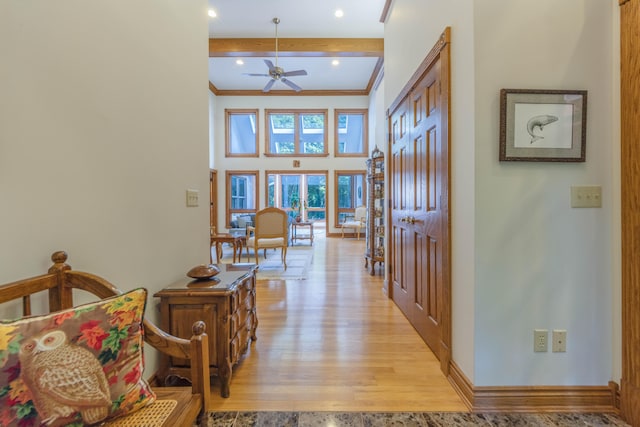 hall featuring beam ceiling, crown molding, light hardwood / wood-style floors, and a high ceiling