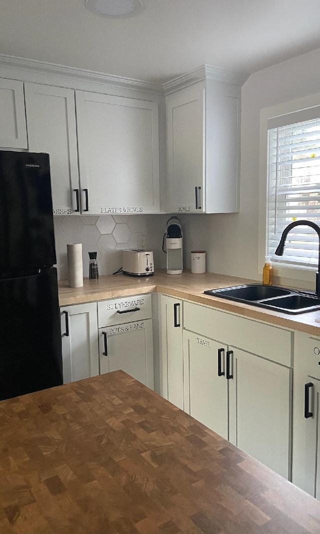 kitchen with white cabinets, decorative backsplash, black fridge, and sink