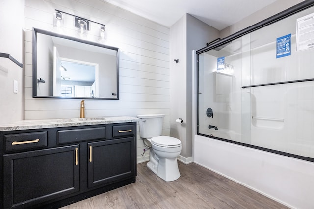 full bathroom with combined bath / shower with glass door, vanity, wooden walls, hardwood / wood-style flooring, and toilet