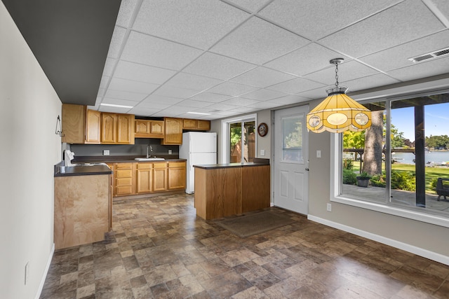 kitchen with dark countertops, freestanding refrigerator, baseboards, and a sink