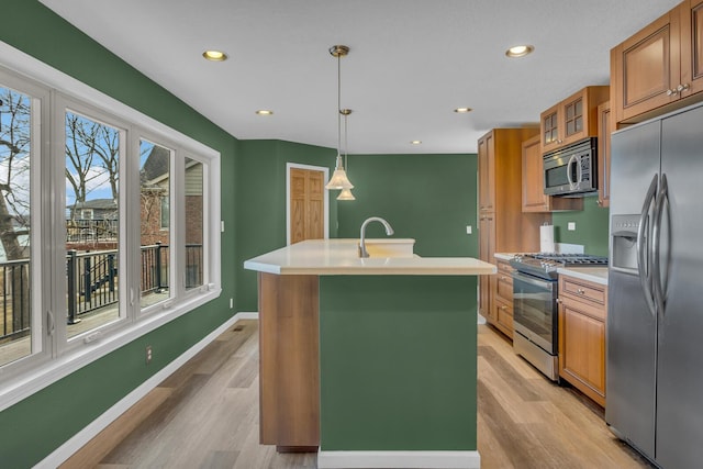 kitchen featuring brown cabinets, an island with sink, a sink, appliances with stainless steel finishes, and light countertops