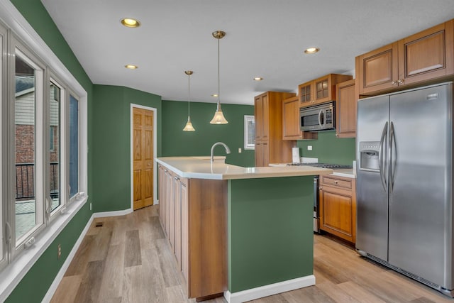 kitchen with light countertops, an island with sink, light wood-type flooring, and appliances with stainless steel finishes