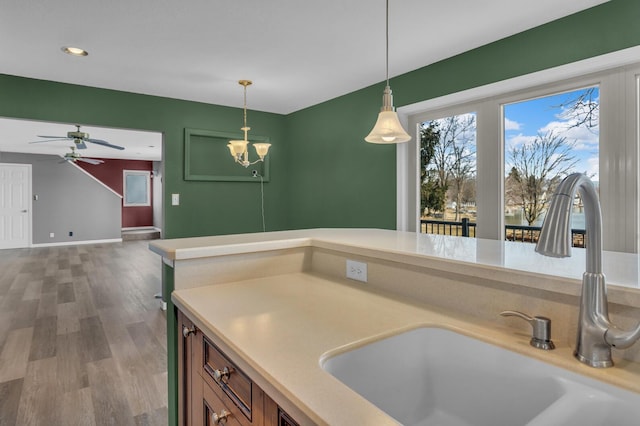 kitchen with pendant lighting, ceiling fan with notable chandelier, a sink, wood finished floors, and light countertops