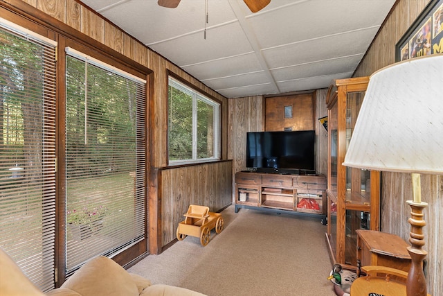 carpeted living room featuring wood walls, a drop ceiling, and ceiling fan