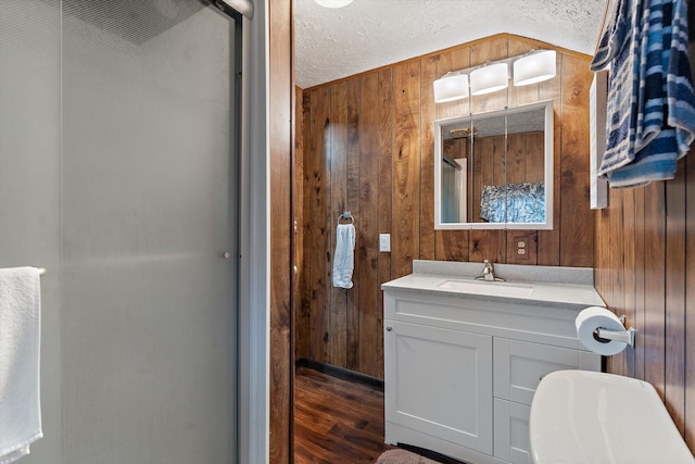 bathroom with hardwood / wood-style floors, vanity, wooden walls, vaulted ceiling, and a textured ceiling