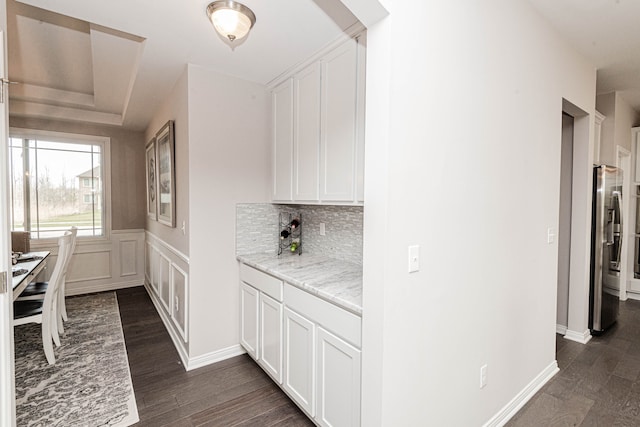 kitchen with dark hardwood / wood-style floors, white cabinetry, stainless steel fridge, decorative backsplash, and light stone counters