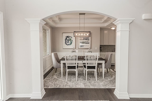 dining area with a tray ceiling, dark hardwood / wood-style floors, and ornate columns