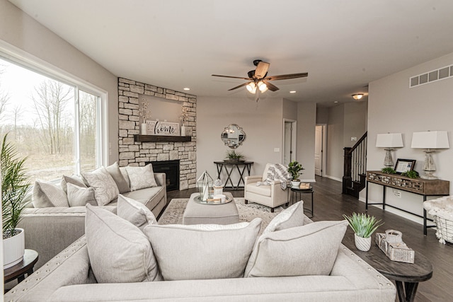 living room featuring a stone fireplace, dark wood-type flooring, and ceiling fan