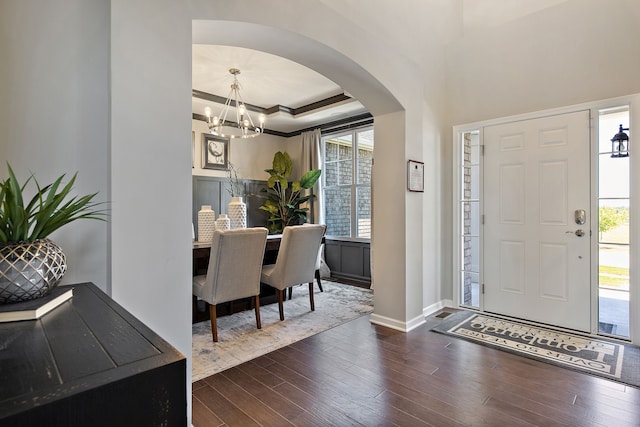 entryway featuring a raised ceiling, an inviting chandelier, ornamental molding, and dark wood-type flooring