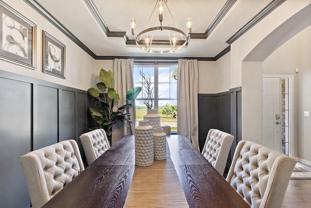 dining room with an inviting chandelier, ornamental molding, a tray ceiling, and light hardwood / wood-style flooring