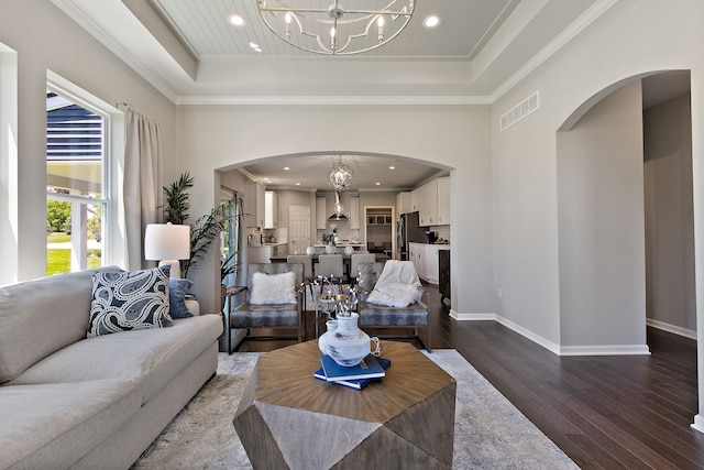 living room featuring hardwood / wood-style flooring, a raised ceiling, crown molding, and a notable chandelier