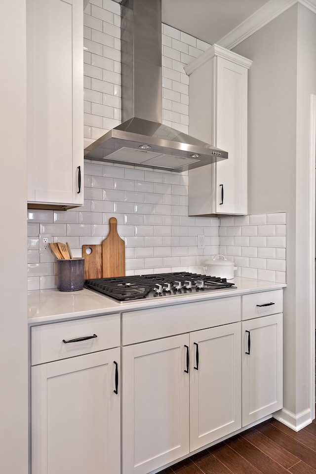 kitchen featuring tasteful backsplash, wall chimney exhaust hood, stainless steel gas cooktop, dark wood-type flooring, and white cabinets