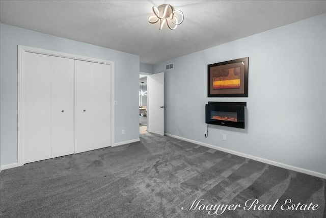 unfurnished bedroom with visible vents, baseboards, a closet, dark colored carpet, and a glass covered fireplace