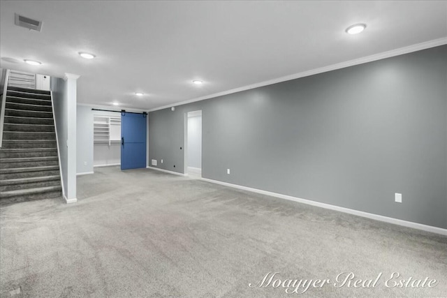 finished below grade area featuring a barn door, visible vents, baseboards, stairs, and crown molding