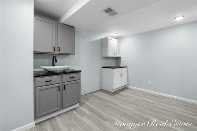 kitchen with dark countertops, gray cabinets, visible vents, and a sink