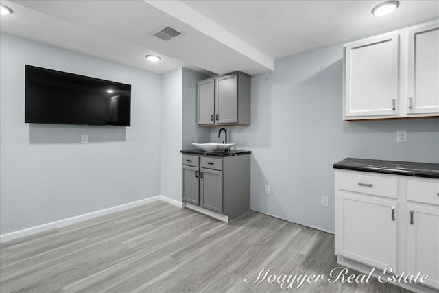 bar featuring light wood-type flooring, a sink, visible vents, and baseboards