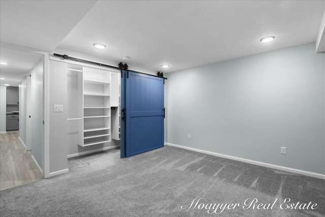 unfurnished bedroom with a barn door, carpet, and baseboards