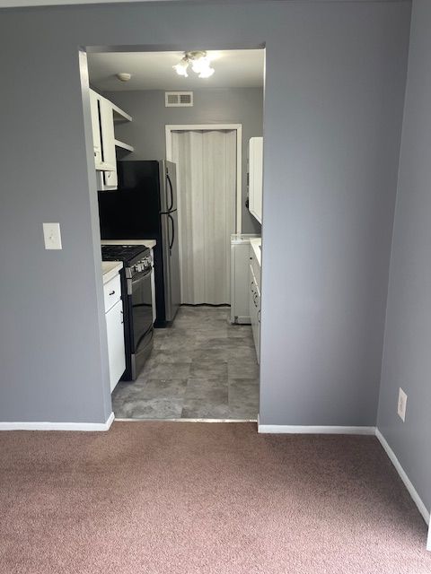 kitchen with range with gas stovetop, white cabinetry, and light carpet