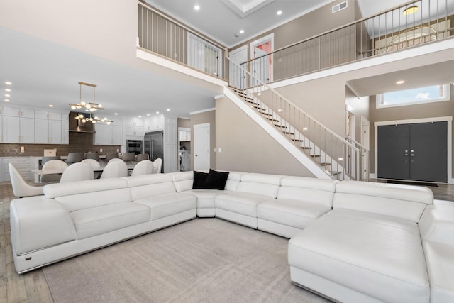 living room featuring light wood-type flooring, a towering ceiling, and a notable chandelier