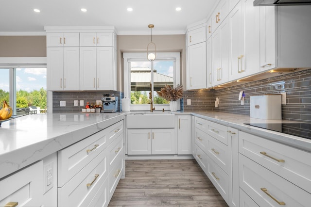 kitchen with light stone countertops, crown molding, white cabinets, and a healthy amount of sunlight