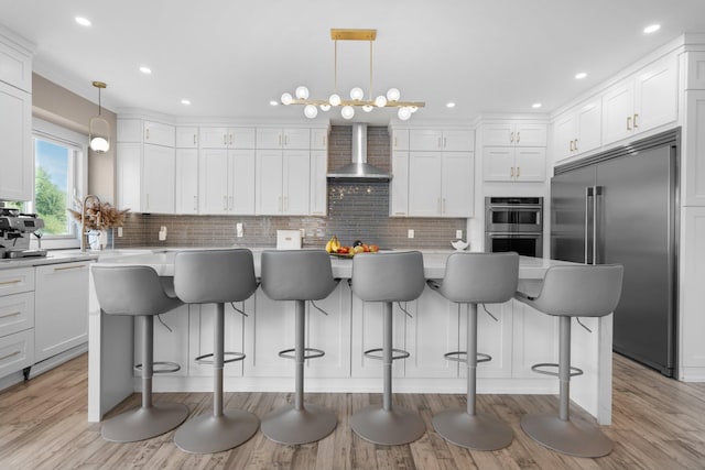 kitchen featuring appliances with stainless steel finishes, a center island, hanging light fixtures, and wall chimney range hood