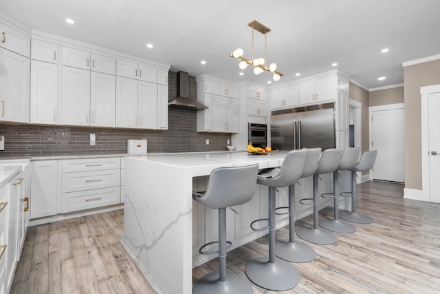 kitchen featuring white cabinetry, a center island, wall chimney exhaust hood, pendant lighting, and appliances with stainless steel finishes