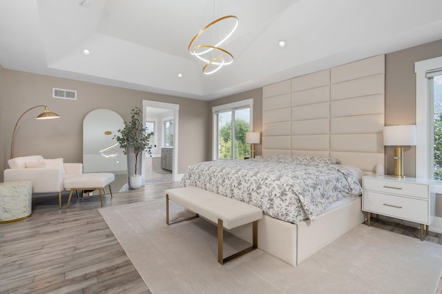 bedroom with a notable chandelier, ensuite bathroom, light hardwood / wood-style floors, and a raised ceiling