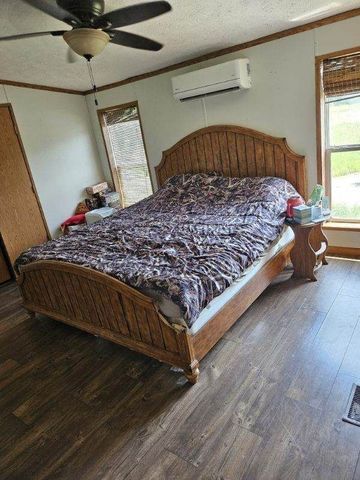 bedroom featuring an AC wall unit, ceiling fan, dark hardwood / wood-style floors, ornamental molding, and a textured ceiling